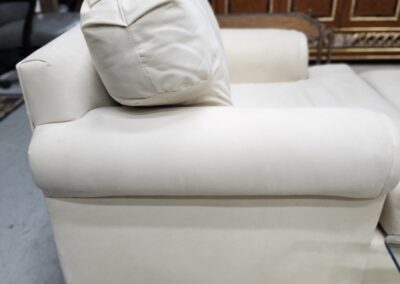 A white cushioned armchair with a wrinkled pillow on it.