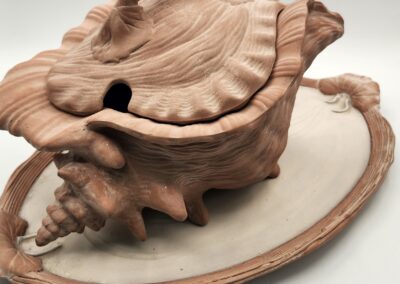 Handcrafted clay teapot with a seashell design on a matching tray.