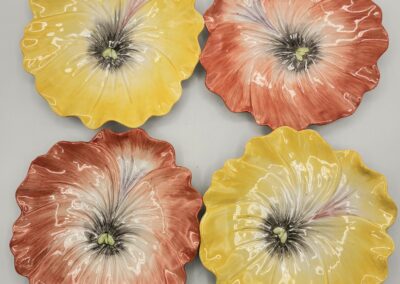 Four colorful ceramic plates shaped like flowers with yellow and red hues.