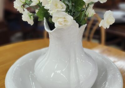 White flowers in a white ceramic vase on a matching plate.