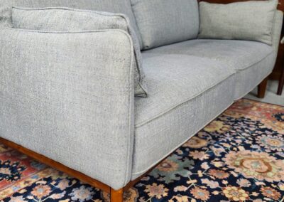 Modern gray fabric sofa with wooden legs on a floral rug.