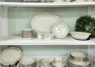 Elegant white dinnerware with gold trim displayed on shelves.