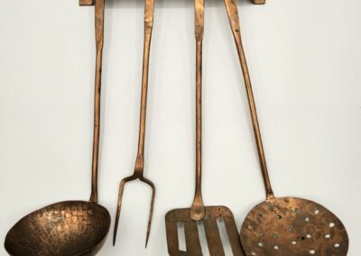 Set of vintage copper kitchen utensils hanging on a wooden rack.