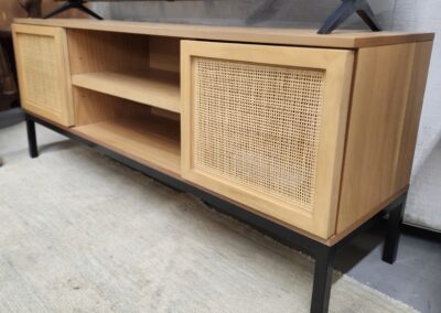 Wooden TV stand with woven rattan doors and black metal legs.
