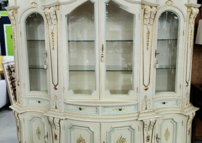Antique cream-colored display cabinet with glass doors and intricate carvings.