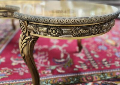 Ornate round wooden table with intricate gold detailing and carved legs on a patterned rug.