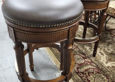 Round wooden bar stools with dark leather seats and ornate legs.