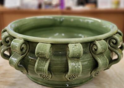 Green ceramic pot with ornate handles on a wooden surface.