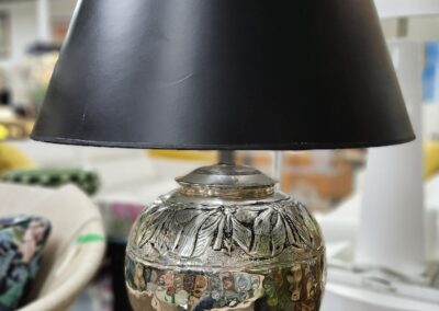 A decorative table lamp with a black shade and ornate silver base.