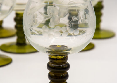 Elegant wine glasses with etched floral designs and green stems.