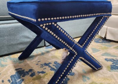 Blue velvet stool with X-shaped legs and studded detailing.