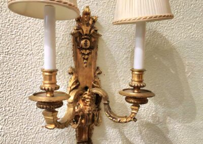 Ornate vintage brass wall sconce with two lamps and cream lampshades.