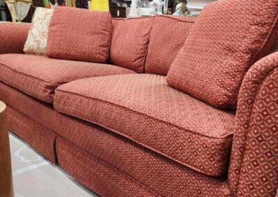 A cozy red fabric sofa with three cushions in a well-lit room.