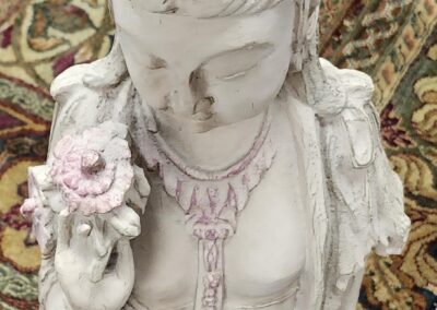 Close-up of a delicate white statue holding a flower, adorned with pink details.