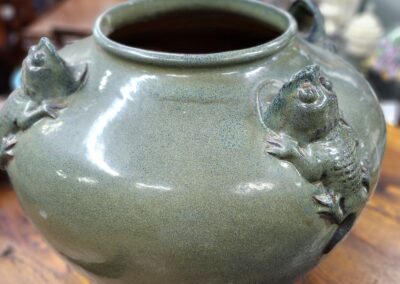 A green ceramic vase with detailed floral decorations on a wooden table.