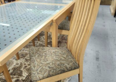Wooden chair with patterned cushion next to glass table in a furniture store.