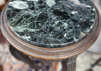 Round table with a dark green marble top and wooden legs.
