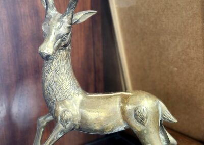 A brass deer statue with detailed antlers and a poised stance on a wooden surface.
