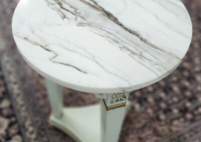 Round marble-top side table with a green base on a patterned rug.