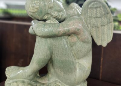 A green angel statue sitting with head resting on knees.