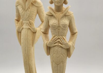 Two elegant wooden female figurines with detailed attire and hats.