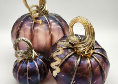 Three decorative pumpkins with elegant metallic wire designs in purple and gold tones.