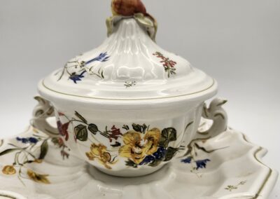 Ornate floral porcelain tureen with lid and detailed scalloped base.