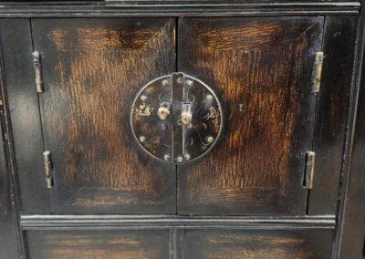 Antique wooden cabinet with intricate metal circular handle and drawers.