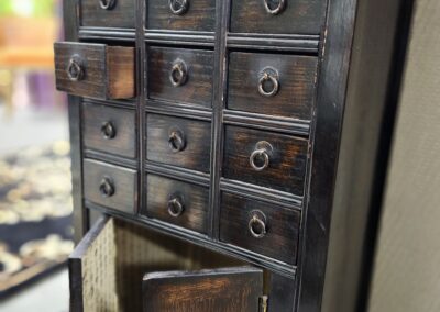 Vintage wooden cabinet with small drawers and one open door.