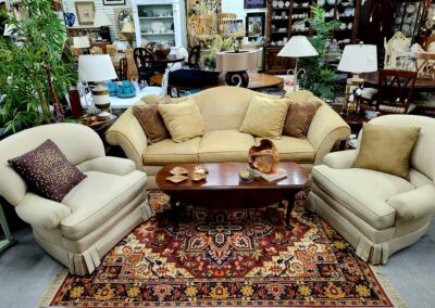 Cozy living room set with beige sofa and armchairs around a wooden coffee table on a patterned rug.