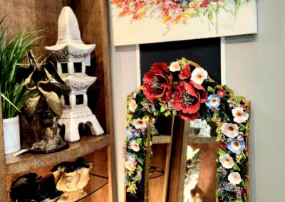 Decorative mirror with floral frame and artistic elements on a wooden shelf.