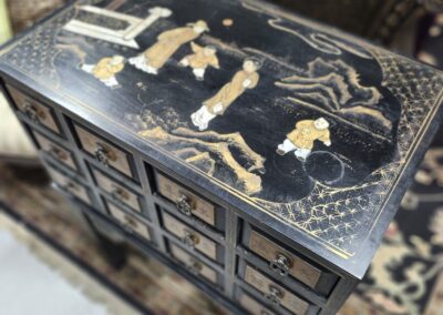 Ornate black lacquer cabinet with gold Asian-inspired designs and multiple small drawers.