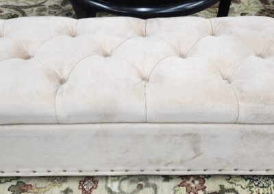 Beige tufted ottoman on patterned rug.