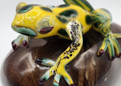 Colorful glass frog on smooth brown stone.
