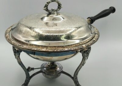 Ornate silver chafing dish with wooden handle.