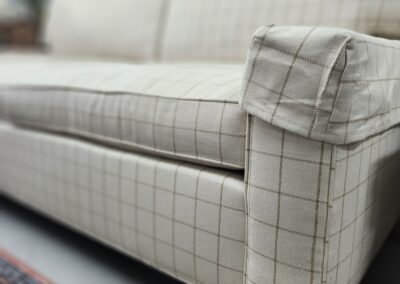 Plaid sofa with wooden legs on rug.