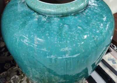 Large turquoise ceramic vase on patterned rug.