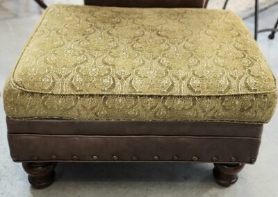 Ornate upholstered ottoman with wooden legs.