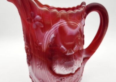 Red glass pitcher with intricate floral design.