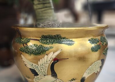 Golden pot with painted cranes and trees.