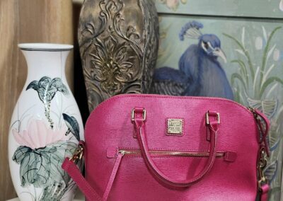 Pink handbag on white dresser near vases.