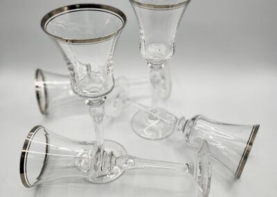 Six clear wine glasses with silver rims.