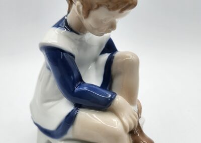 Porcelain figurine of girl sitting on stool.