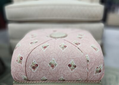 Pink ottoman with tassels in front chair.