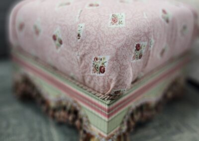 Pink floral ottoman with decorative fringe.