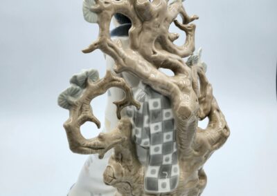 Ceramic figurine behind a detailed tree sculpture.
