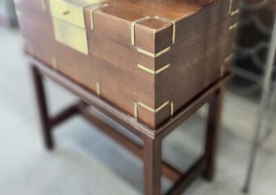 Wooden chest with brass accents on stand.