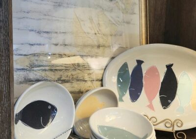 Ceramic fish plates displayed on wooden shelf.