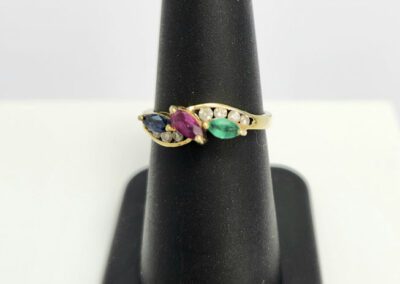 Gold ring with colorful gemstones on stand.