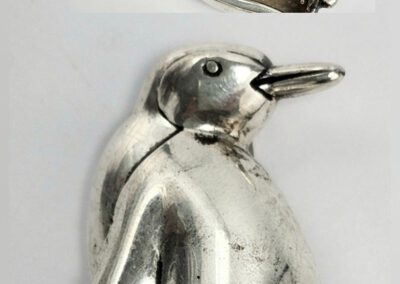 Silver penguin-shaped metal object, two views.